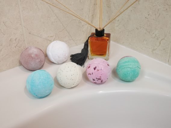 bombe de bain se diluant entouré de pétales de fleur et la main d'une femme caressant l'eau