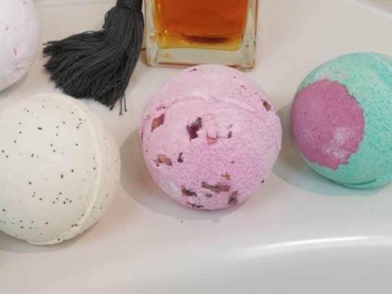 bombe de bain se diluant entouré de pétales de fleur et la main d'une femme caressant l'eau