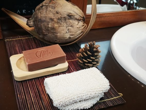 bombe de bain se diluant entouré de pétales de fleur et la main d'une femme caressant l'eau