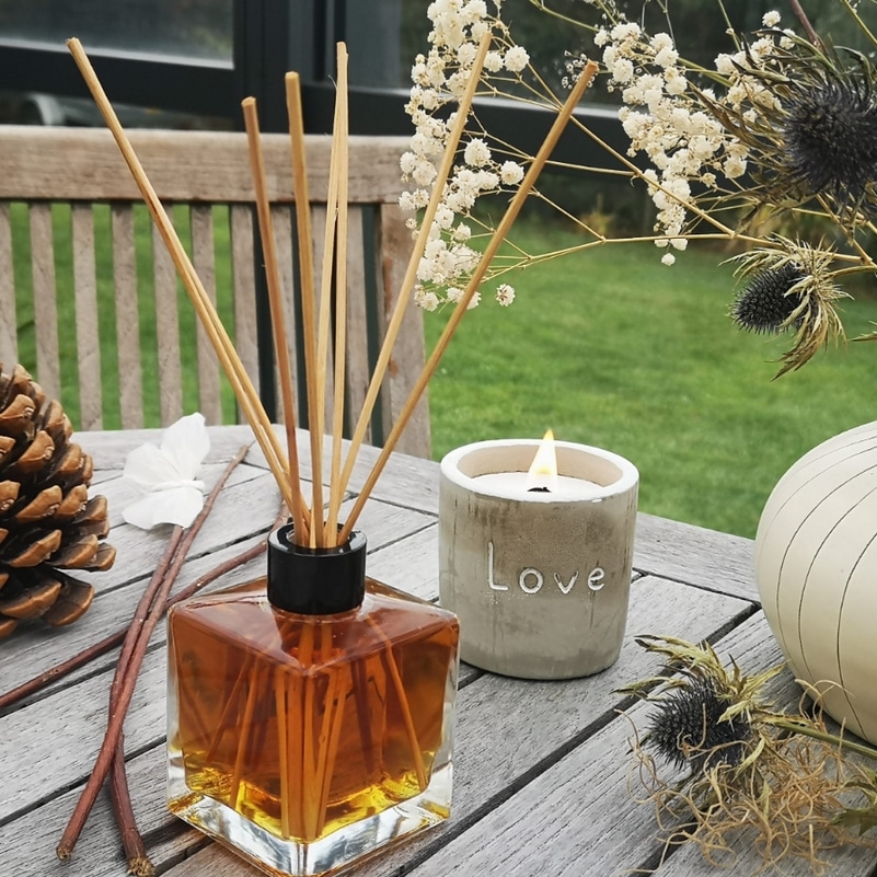 Bougie béton et un diffuseur de parfum patchouli en ambiance sur une table en bois de jardin