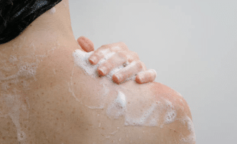 une femme se lavant et passant sa main sur l'épaule avec du savon moussant