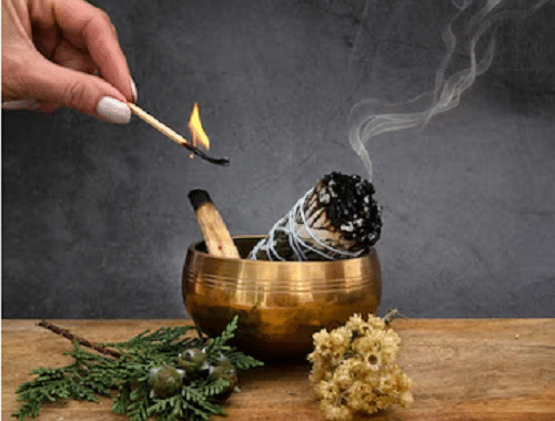 dans un bol en cuivre, melange d'une sauge et d'un palo santo avec une main qui les allume