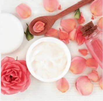 récipient de crème et cuillère en bois accompagnés de pétales de rose