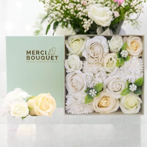 boîtes cadeaux rondes de fleurs de savon ivoire blanc posée sur une table marbrée blanche