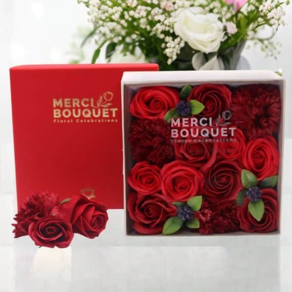 boîtes cadeaux rondes de fleurs de savon rouge posée sur une table marbrée blanche